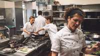 Drei Frauen und ein Mann arbeiten sichtlich unter Druck in einer Profi-Küche