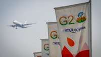 G20-India-Fahnen in Reihe vor einem Himmel, auf dem ein Flugzeug zu sehen ist