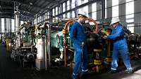 Ausbilder und Azubi arbeiten zusammen an einer Maschine. 
