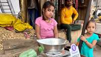Zwei indische Mädchen verkaufen Erdnüsse, an der Waage lehnt ein Schild mit QR-Code