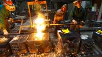 Arbeiter gießen flüssiges Metall in Kokillen 
