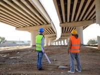 Männer in Sicherheitswesten, vermutlich Ingenieure, stehen unter dem Rohbau einer Brücke