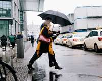Businessmäßig gekleidetes Paar mit Schrim tritt im Regen auf die Straße zu einem Taxistand
