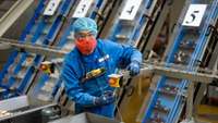 Techniker im Blaumann mit Schutzmaske und Haarnetz an einer Produktionsanlage mit Waffeln
