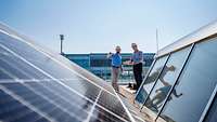 Zwei Männer stehen auf dem Dach und kontrollieren Solarpanels