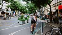 Radfahrerin auf begrünter Einkaufsstraße