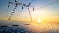 Hochspannungsleitung über Solarpanelen im Morgenlicht