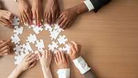 viele Hände, deren Besitzer offenbar unterschiedlichen Ethnien angehören, verschieben Puzzleteile auf einem Tisch
