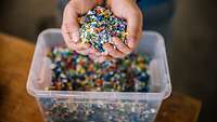 Hände greifen in eine Plastikbox mit Kunststoffgranulat