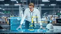 Innovative Wirtschaft Mann stehet in einer Fabrik vor dem Hologramm eines Roboterarms