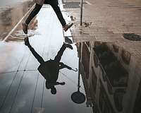 Mensch springt über und spiegelt sich in einer Pfütze auf der Straße 