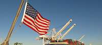 Frachter liegt an einem Hafenkai mit Kränen; im Vordergrund eine US-Flagge