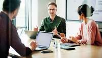 Drei Personen sitzen mit Laptops in einer Besprechung