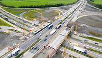 Luftbild mit Blick auf eine Autobahnbaustelle, bei der eine parallele Brücke über einem Verkehrsknoten errichtet wird