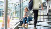 Junge Frau sitzt auf einer Treppe am Campus und sinniert traurig vor sich hin 