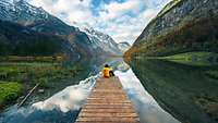 Person sitzt auf einem Steg an einem Bergsee
