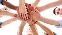 Junge Menschen im Kreis legen in der Mitte ihre Hände übereinander, von unten fotografiert