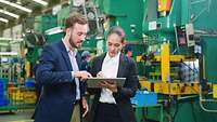 Zwei Personen stehen in der Produktionsstätte und planen auf einem Tablet