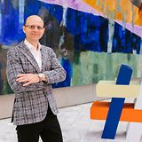 Mann steht vor Gemälde und hat die Arme verschränkt.