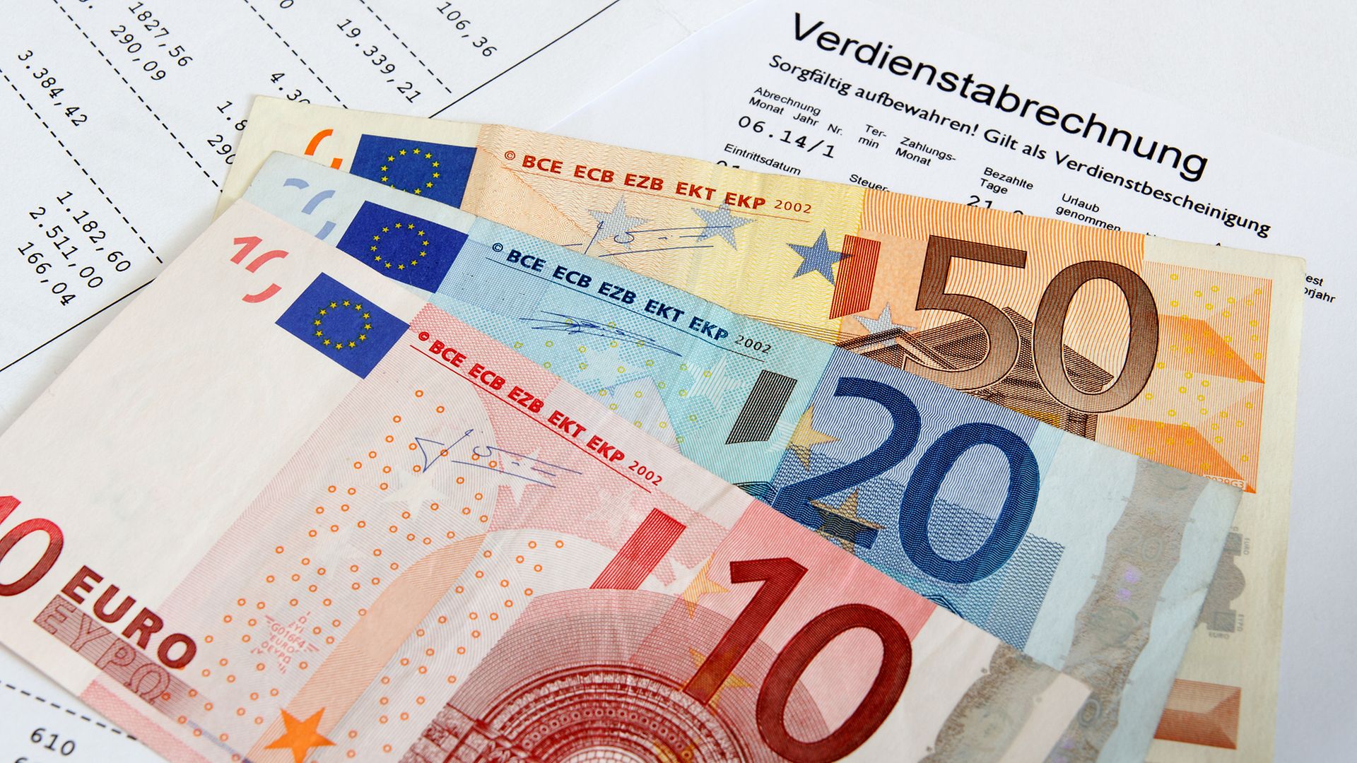 Verdienstabrechnung bedeckt mit mit 10-, 20- und 50-Euro-Banknoten