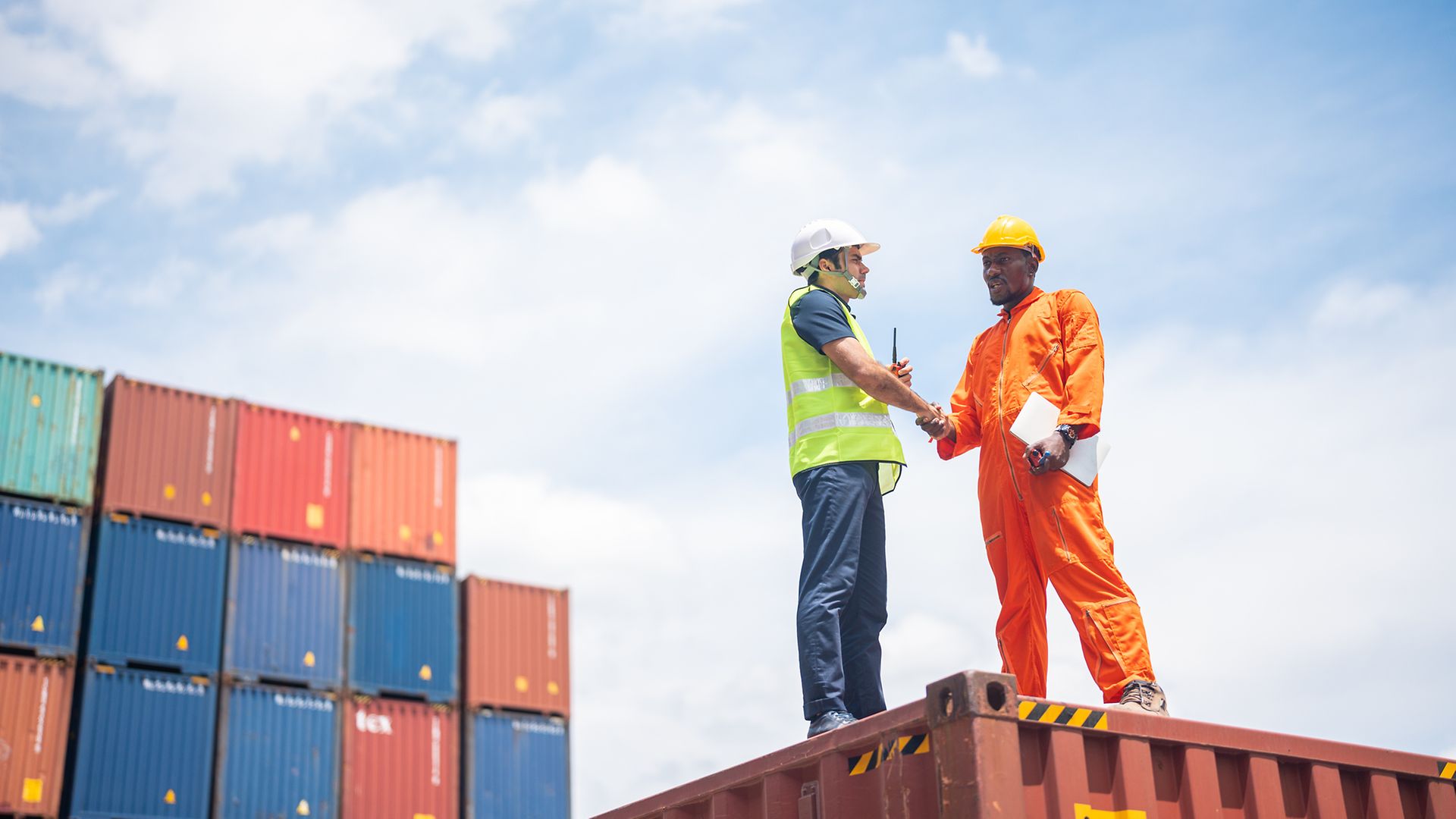 Schwarzer und weißer Arbeiter schütteln sich auf einem Containerstapel die Hände