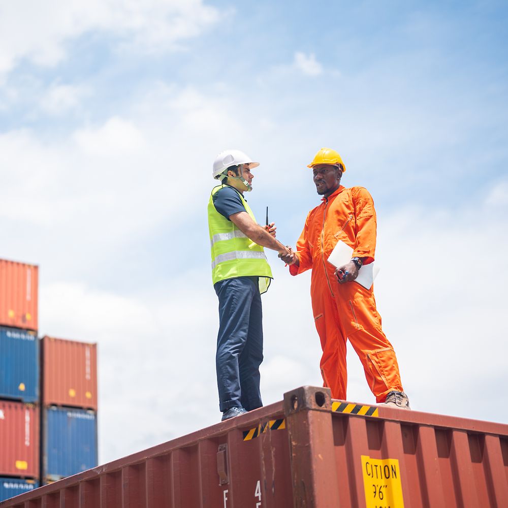 Schwarzer und weißer Arbeiter schütteln sich auf einem Containerstapel die Hände