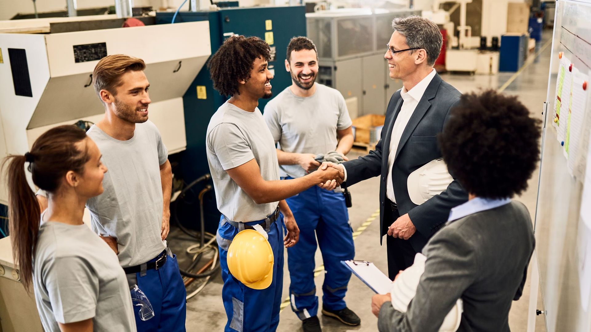 Eine gemischte Gruppe an Facharbeitern steht zusammen und der Chef schüttelt einem schwarzen Mitarbeiter die Hand