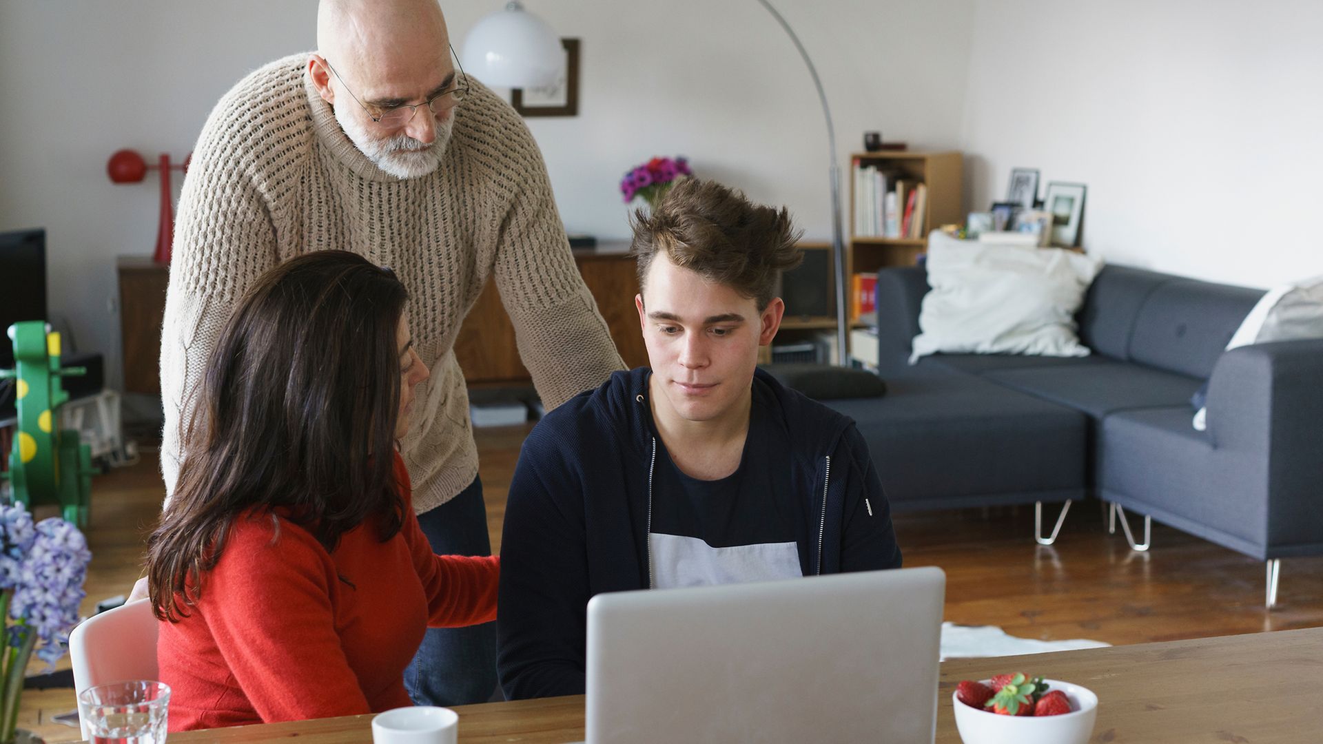 Jugendlicher und Eltern im Wohnzimmer vor einem Laptop