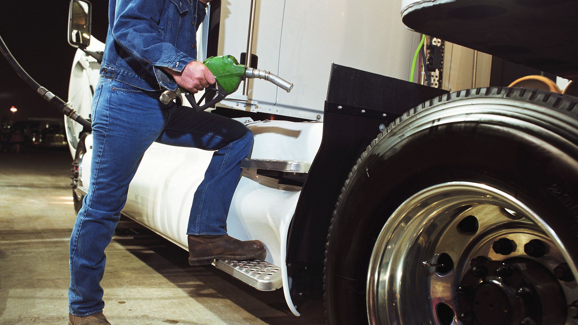 Mann mit Zapfhahn steht am Einfüllstutzen seines LKW an der Tankstelle