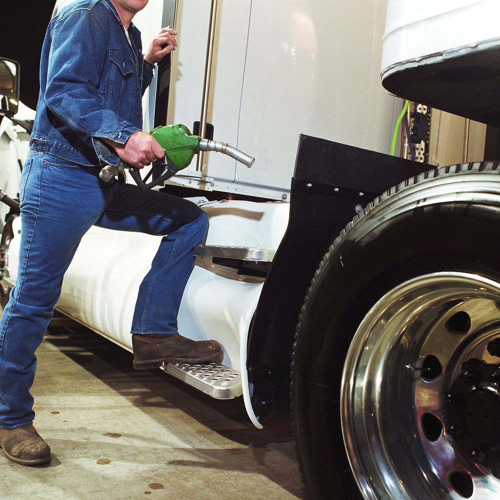 Mann mit Zapfhahn steht am Einfüllstutzen seines LKW an der Tankstelle