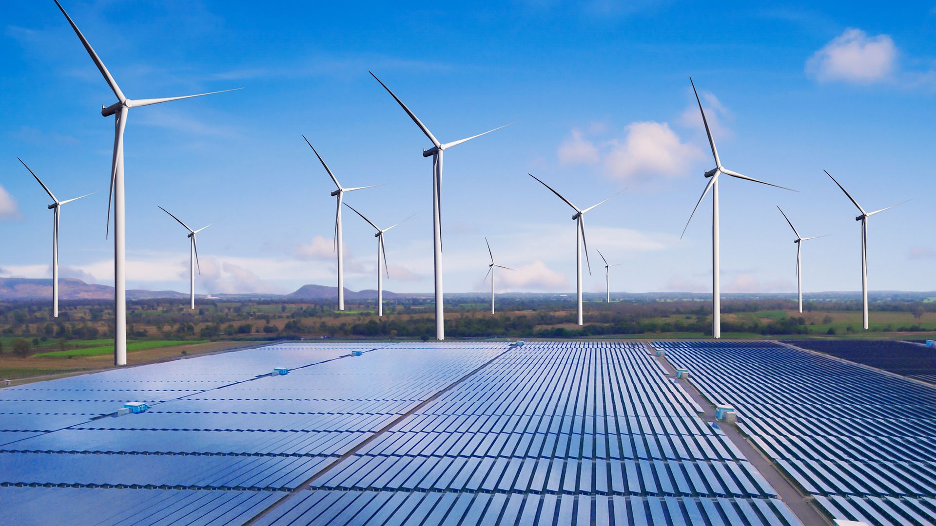 Windräder und Solarpanels vor blauem Himmel