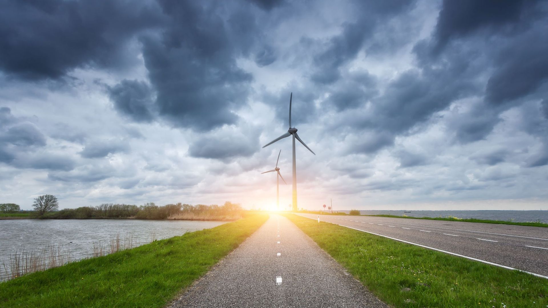 Zwei Wege und eine Wasserstraße führen in einen Sonnenaufgang mit Windrädern 