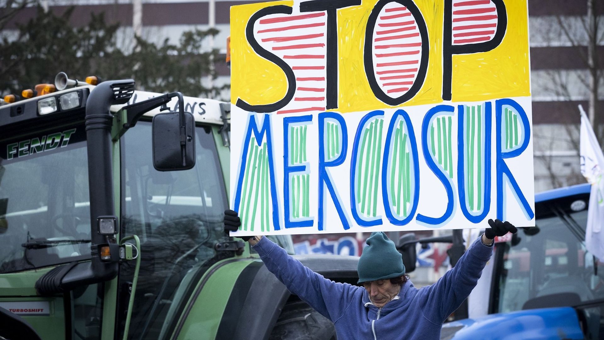 Demonstrant in Brüssel steht mit einem "Stop Mercosur"-Schild vor einem Traktor