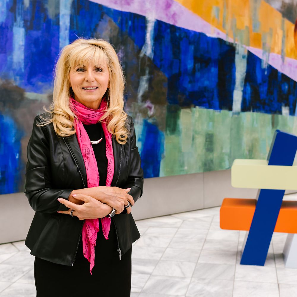 Frau steht vor Gemälde und hat die Arme verschränkt. 