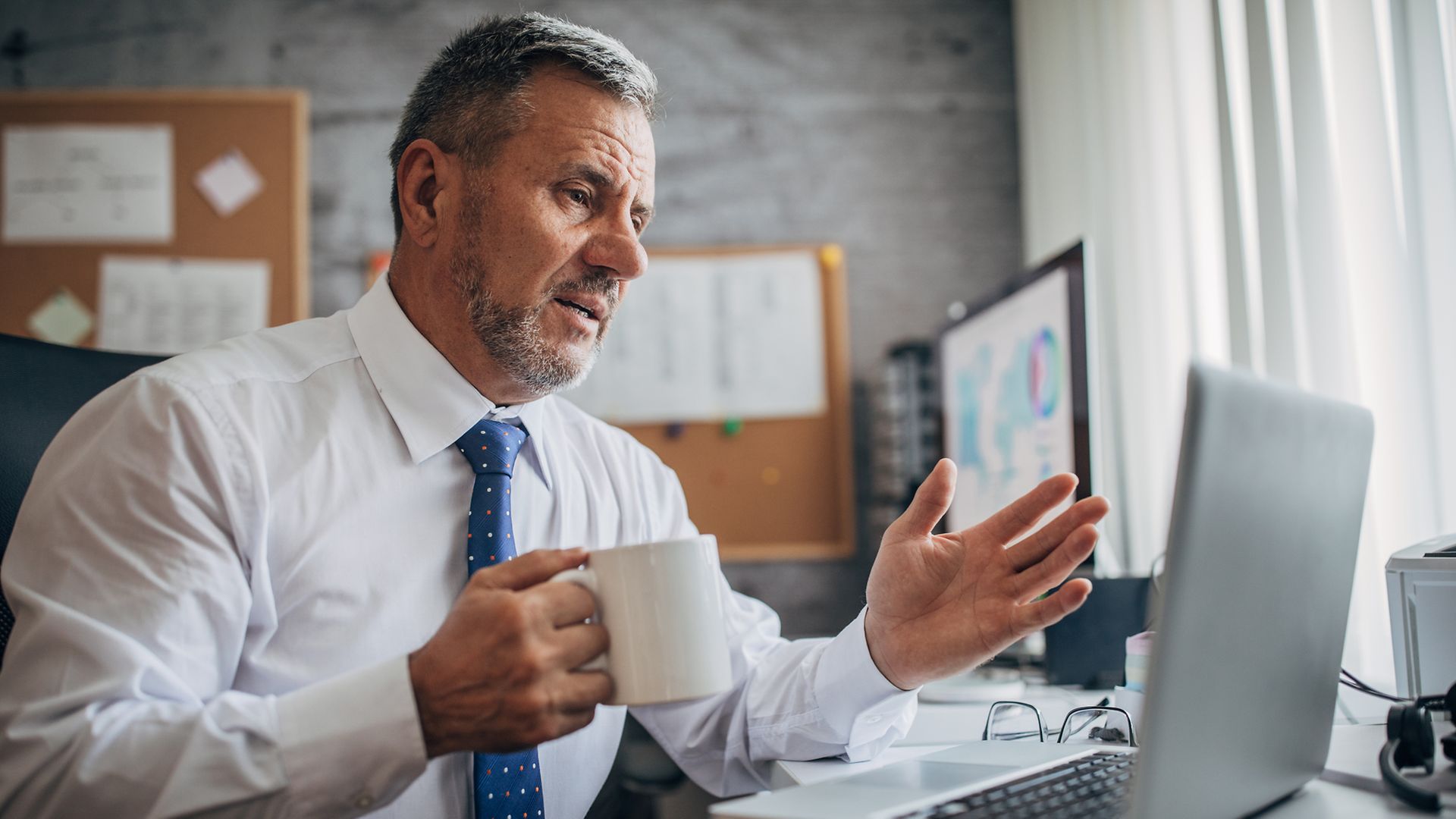 Geschäftsmann am Laptop gestikuliert, eine Tasse in der Hand