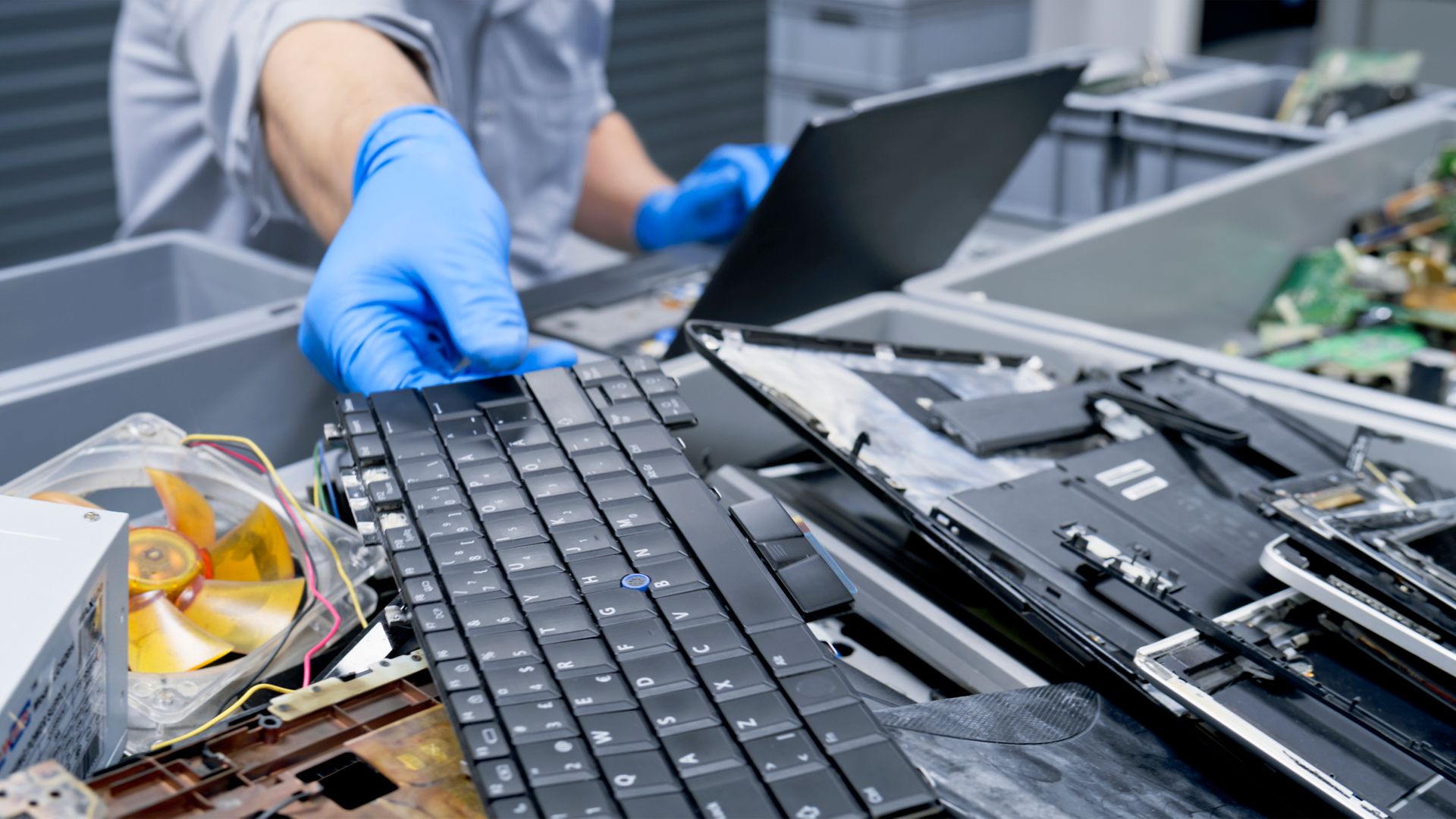 Blau behandschuhte Hand greift nach einer Tastatur im Elektronikschrott