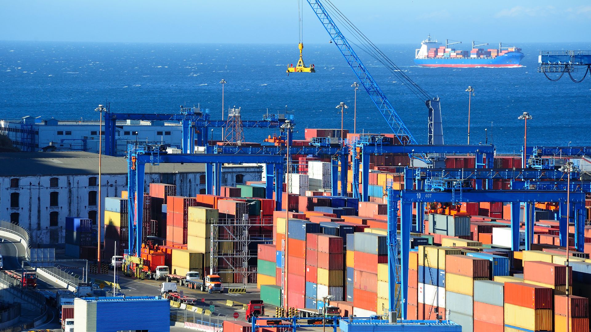 Bunte Container gestapelt, im Hintergrund erkennt man das Meer und ein Transportschiff