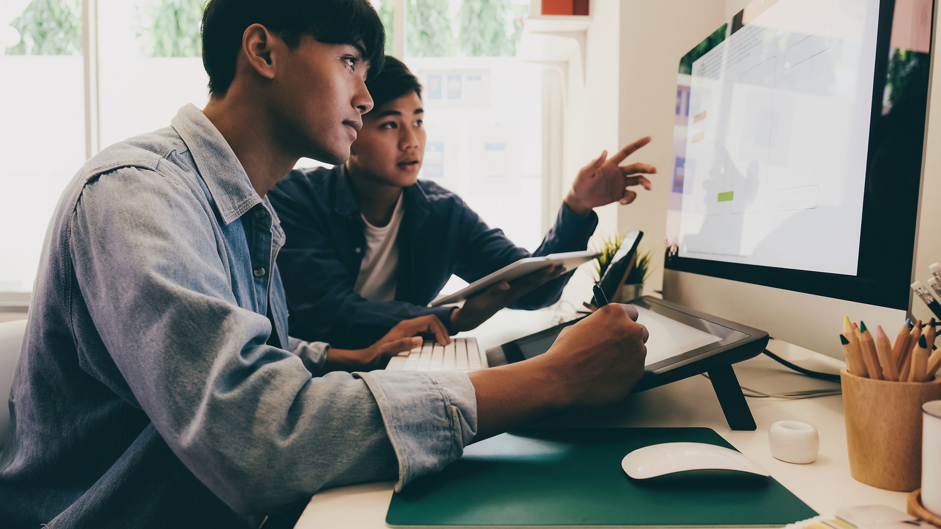 Zwei junge asiatische Männer blicken konzentriert auf einen Computerbildschirm