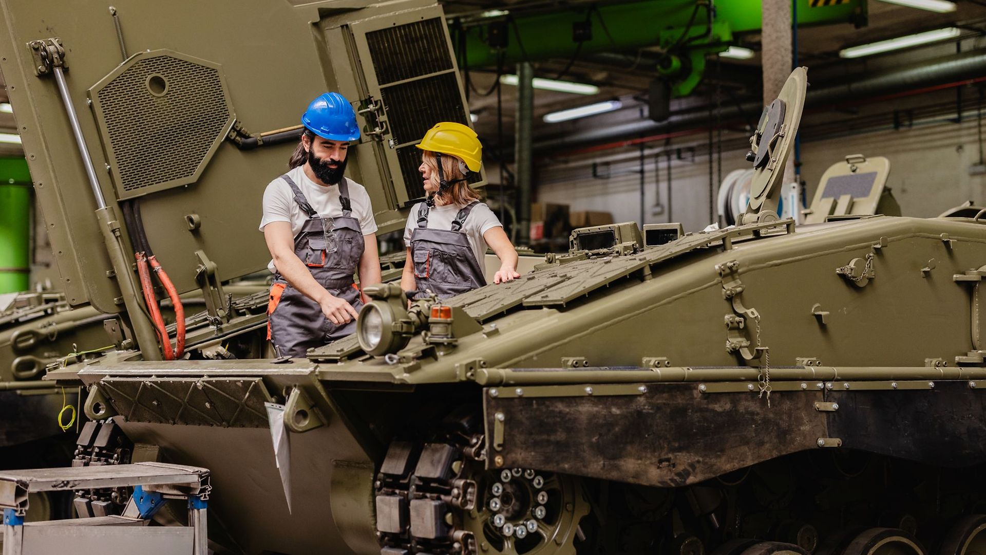 Mechaniker mit Schutzhelmen, eine Frau, ein Mann, arbeiten an einem Panzer