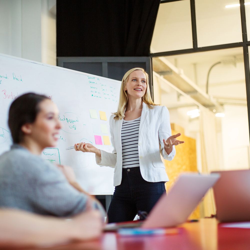 Junge Frau präsentiert etwas vor einem Team an einem Whiteboard