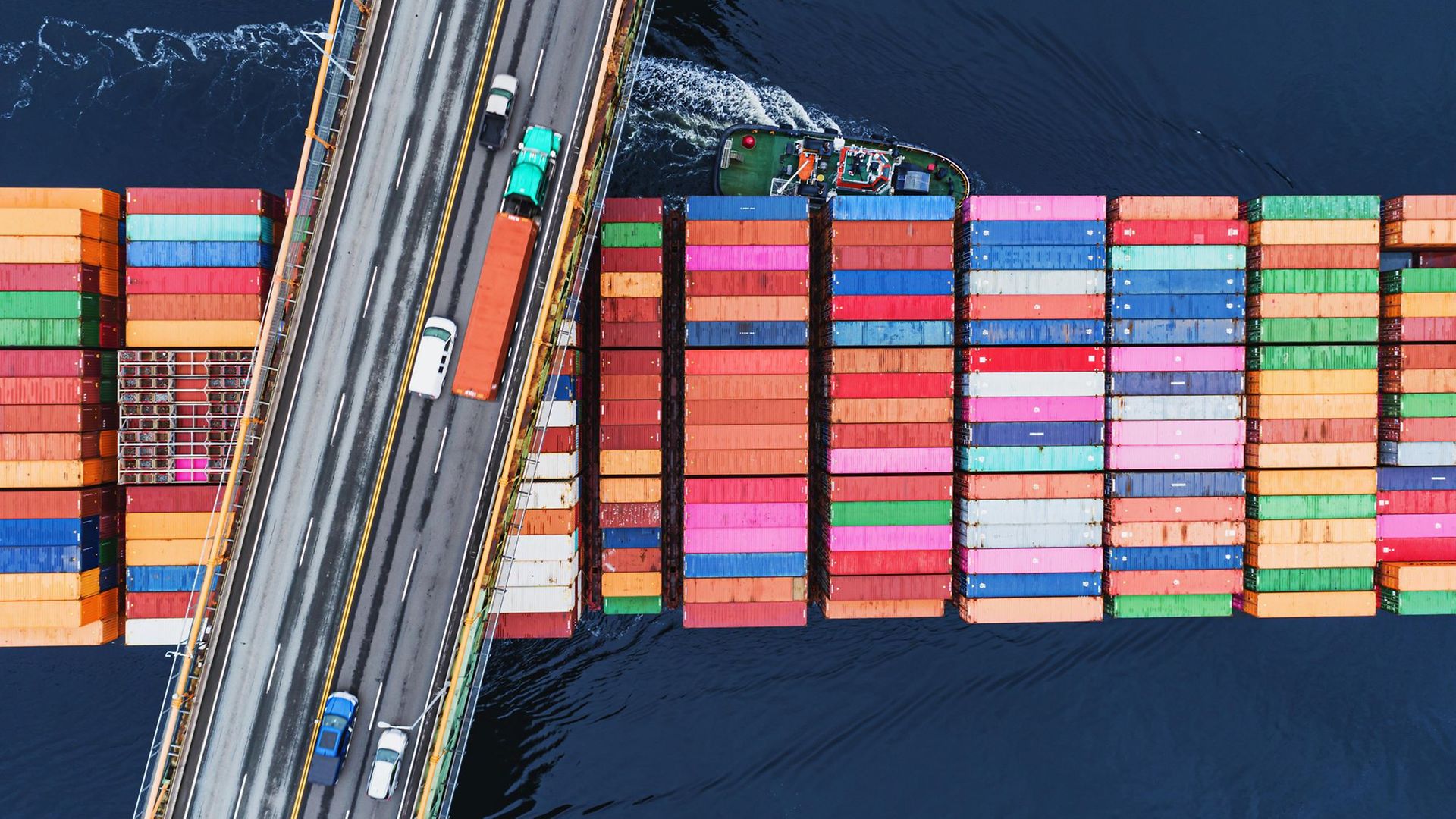 Beladenes Containerschiff unterquert Brücke mit LKW