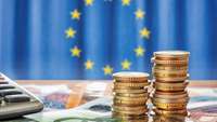 Europaflagge hinter Geldscheinen und Münzstapeln