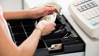 Frau nimmt einen 5-Euro-Schein aus einer recht leeren Ladenkasse