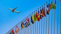 Flugzeug fliegt über eine Reihe Fahnenmasten mit internationalen Flaggen hinweg