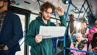 Jugendlicher mit Kopfhörer steht im Bus und studiert die Anzeigen in einer Zeitung