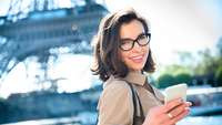 Junge Frau mit Handy vor dem Eiffelturm