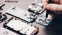 Demontierte Mobilfunktelefone, Hand mit Schraubenzieher schraubt an Platinen