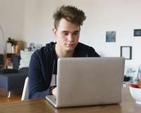 Jugendlicher sitzt an einem Tisch im Wohnzimmer vor einem Laptop