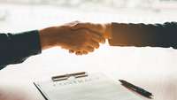 Über einem auf dem Tisch liegenden Vertrag ("Contract") besiegeln zwei Partner die Unterzeichnung mit Händedruck