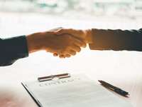Über einem auf dem Tisch liegenden Vertrag ("Contract") besiegeln zwei Partner die Unterzeichnung mit Händedruck
